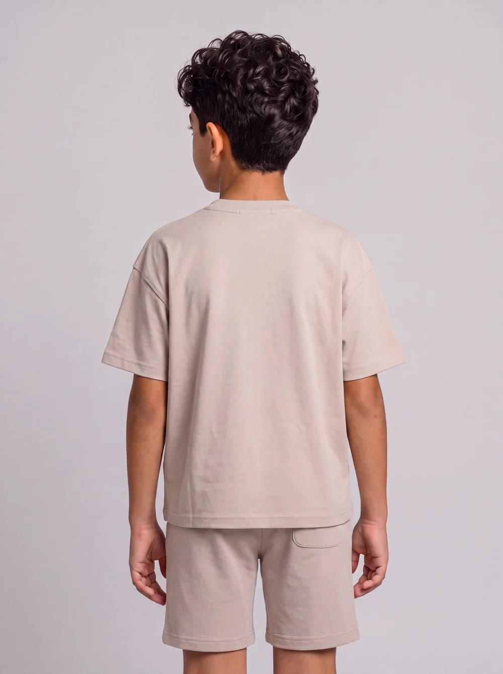 Back-view fashion catalogue image of a child model in a beige outfit.